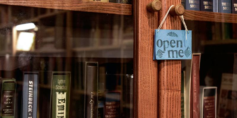 Kuvituskuva. Lasinen kirjakaappi, jossa lukee "open me". 