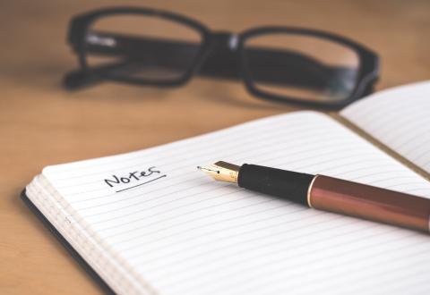 A notebook, a pen and glasses on a table.