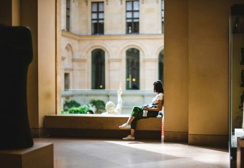 Henkilö istuu ikkunan syvennyksessä ajatuksiinsa uppoutuneena.